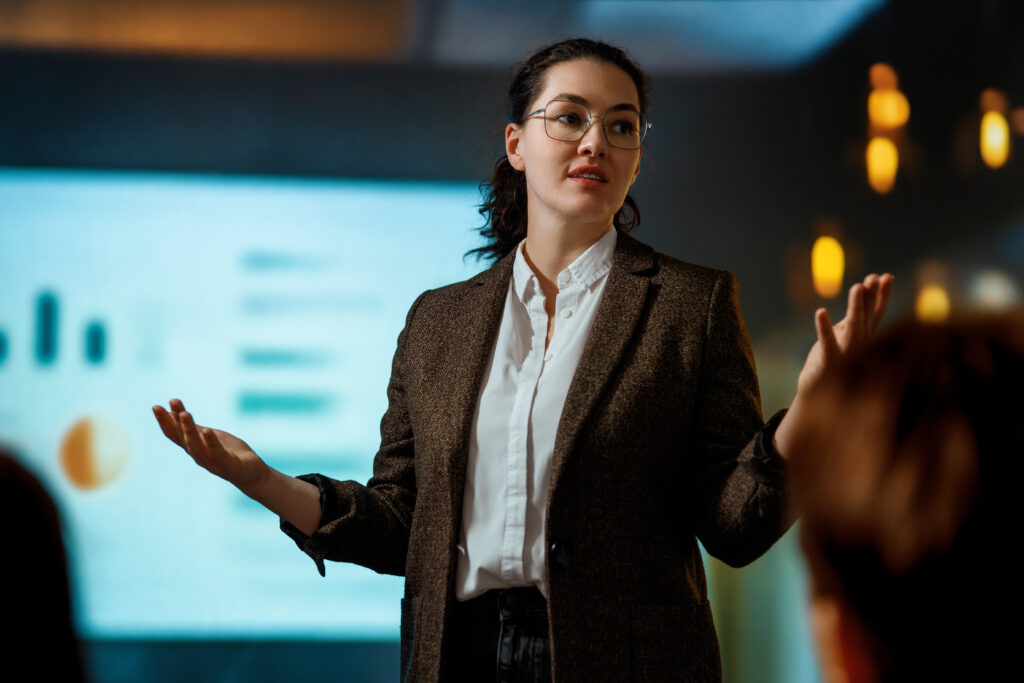 A young professional presenting in front of a screen projection of bars and graphs