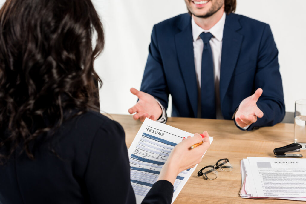 A young man talking to a job interviewer who’s holding a pen and resume